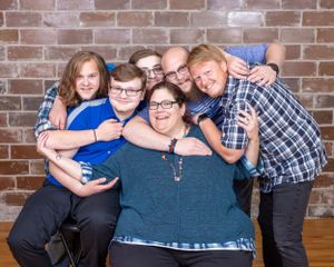 A joyful family of five laughing and embracing together in front of a brick wall backdrop.