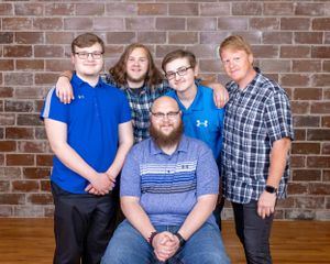 Family portrait of five males posing together against a brick wall, one seated in front.
