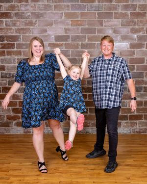 Family of three swinging a young girl between two adults in matching blue floral outfits.