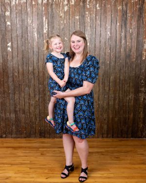 A mother and young daughter wearing matching blue floral dresses pose together for a portrait.