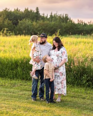 Happy family maternity portrait at sunset, father holding toddler while son touches pregnant mothers belly.