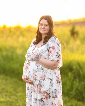 Pregnant woman in white floral maxi dress cradling baby bump during golden hour outdoor maternity session.