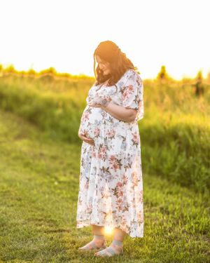 Beautiful pregnant woman in floral dress holding baby bump during stunning golden sunset maternity session.