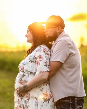 Couple embracing during golden sunset maternity session, man tenderly holding pregnant partners baby bump.