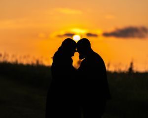 Romantic silhouette of expecting couple touching foreheads against vibrant orange sunset sky.