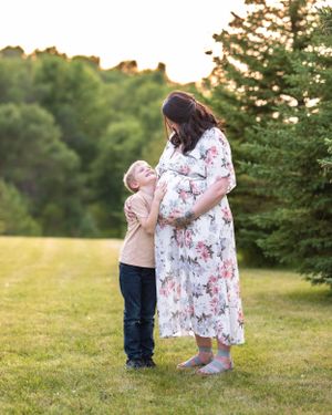 A young boy hugs his pregnant mother in a floral dress during a golden hour maternity photo session outdoors.