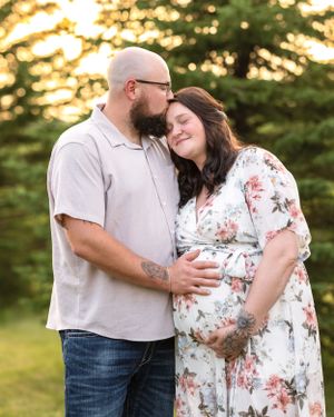 A bearded man kisses his pregnant partner on the forehead during a warm sunset maternity photo session.