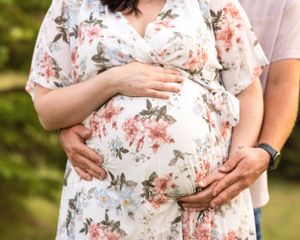Close-up of a pregnant belly in a floral dress with two pairs of hands cradling it during a maternity shoot.