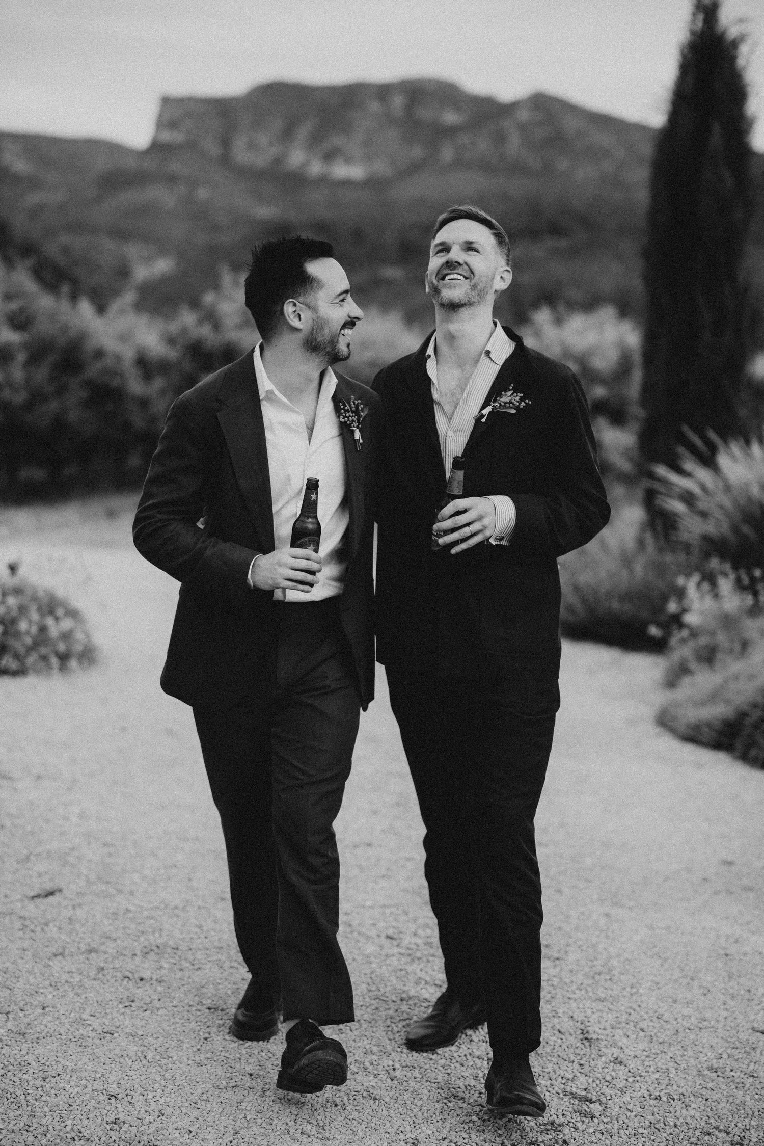 A newlywed couple walks hand in hand on a garden path during golden hour.