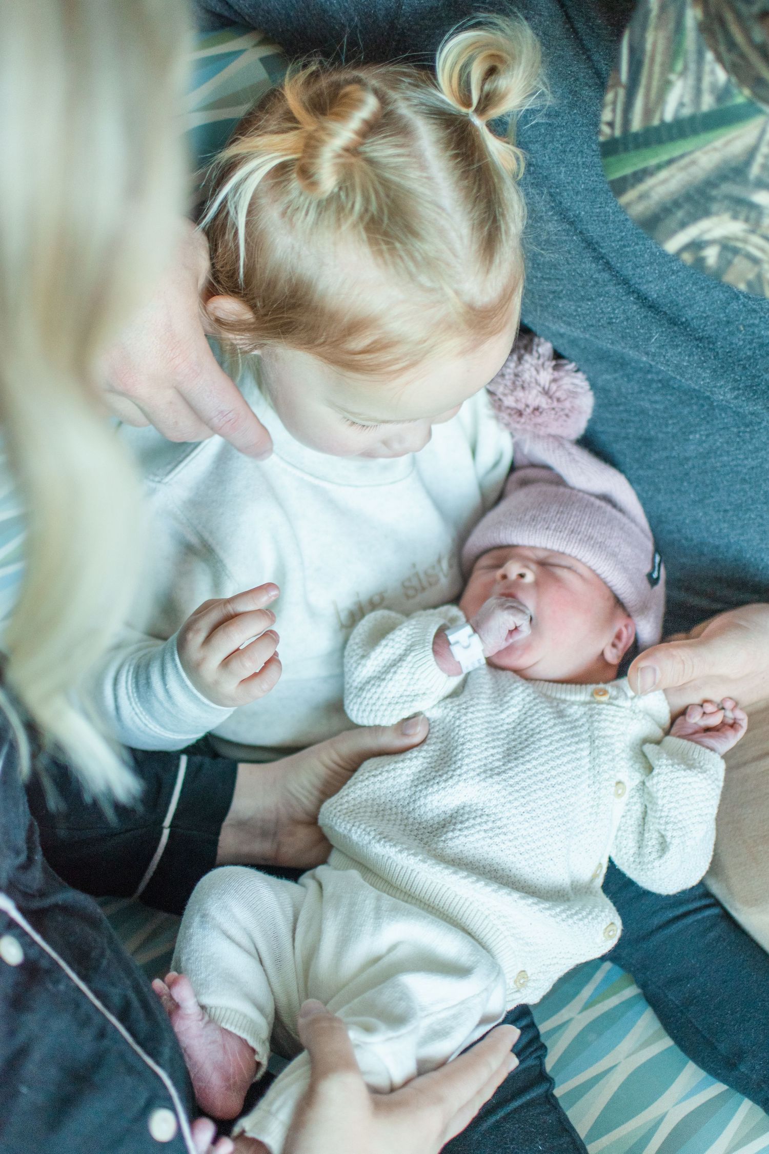 Toddler sitting with sleeping newborn baby wearing matching white outfits.