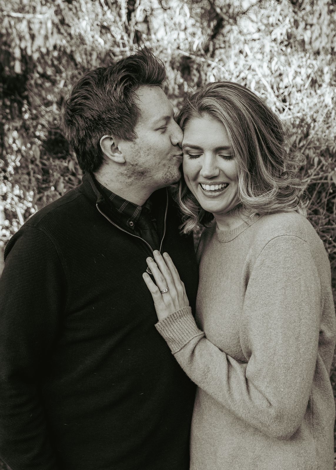 A romantic black and white portrait of a couple sharing a tender moment outdoors.