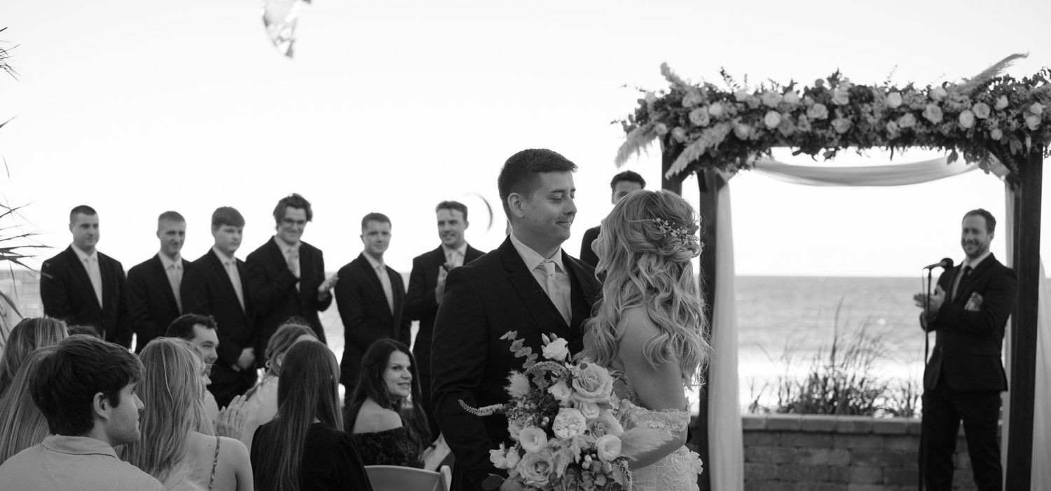Candid moment of a couple walking down the aisle after being married with a person parasailing in the background in Florida