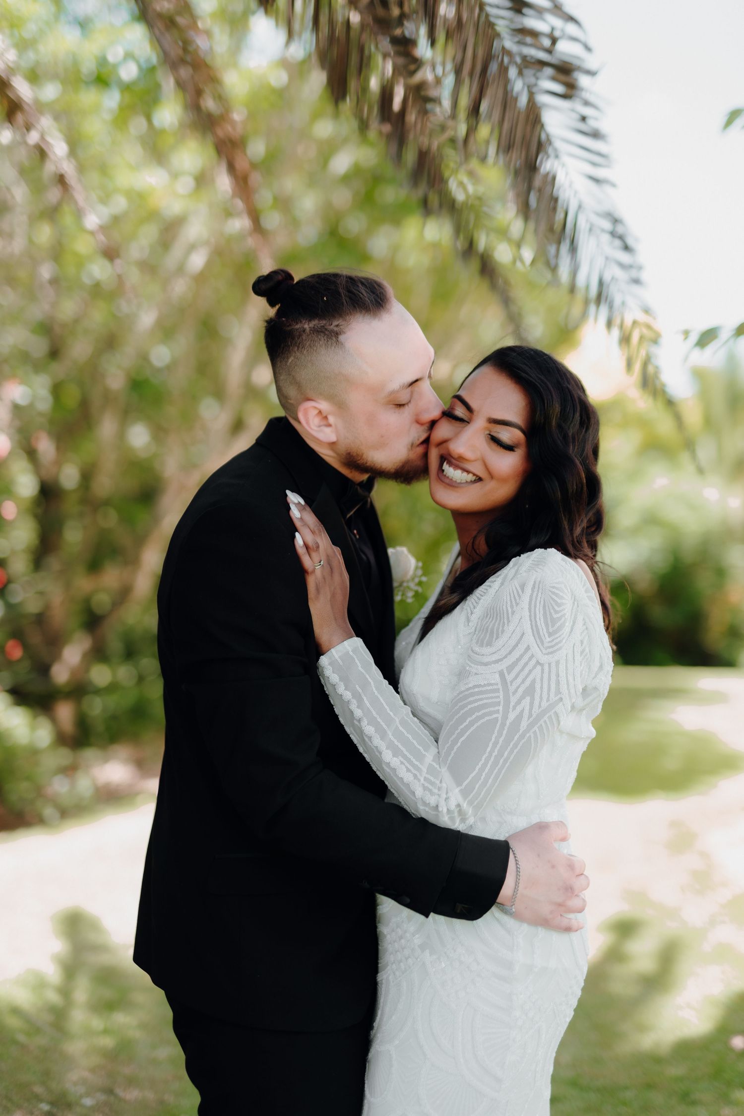 Romantic couple sharing a kiss during their wedding photoshoot in a tropical garden setting.