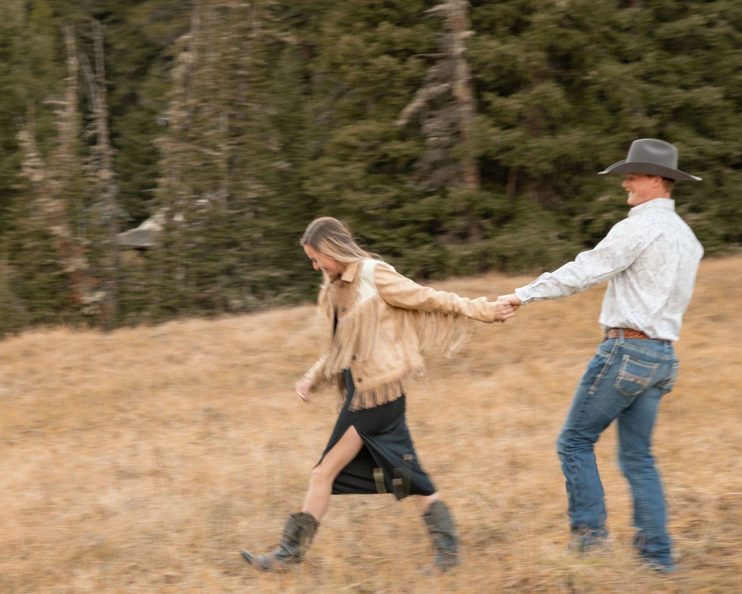 People dancing and spinning together on a dirt path surrounded by evergreen forest.