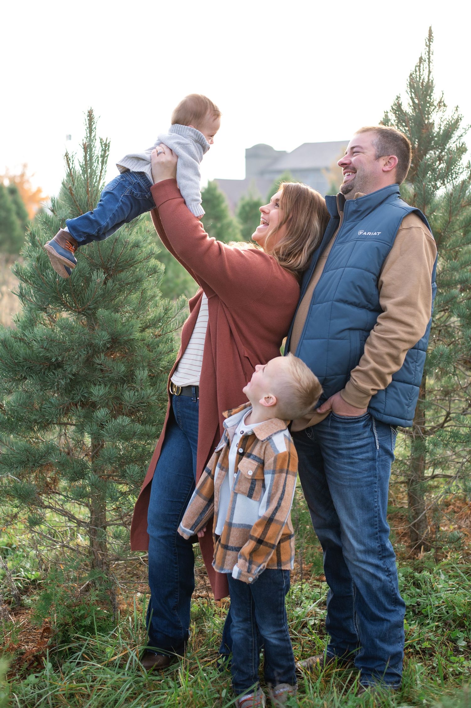A family shares a joyful moment together among evergreen trees during a photo shoot.