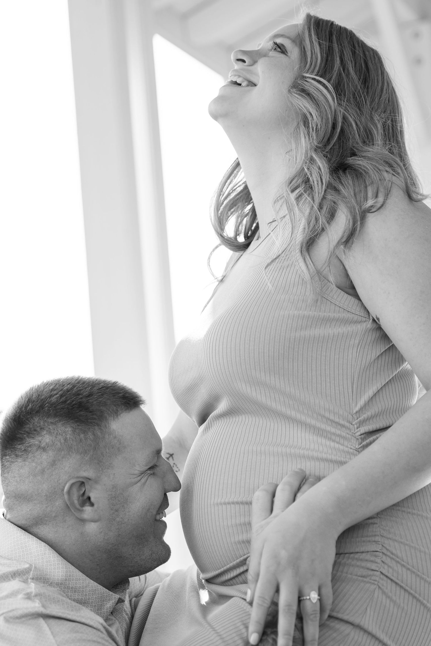 Black and white photo of expectant couple sharing tender moment, man smiling at pregnant belly.