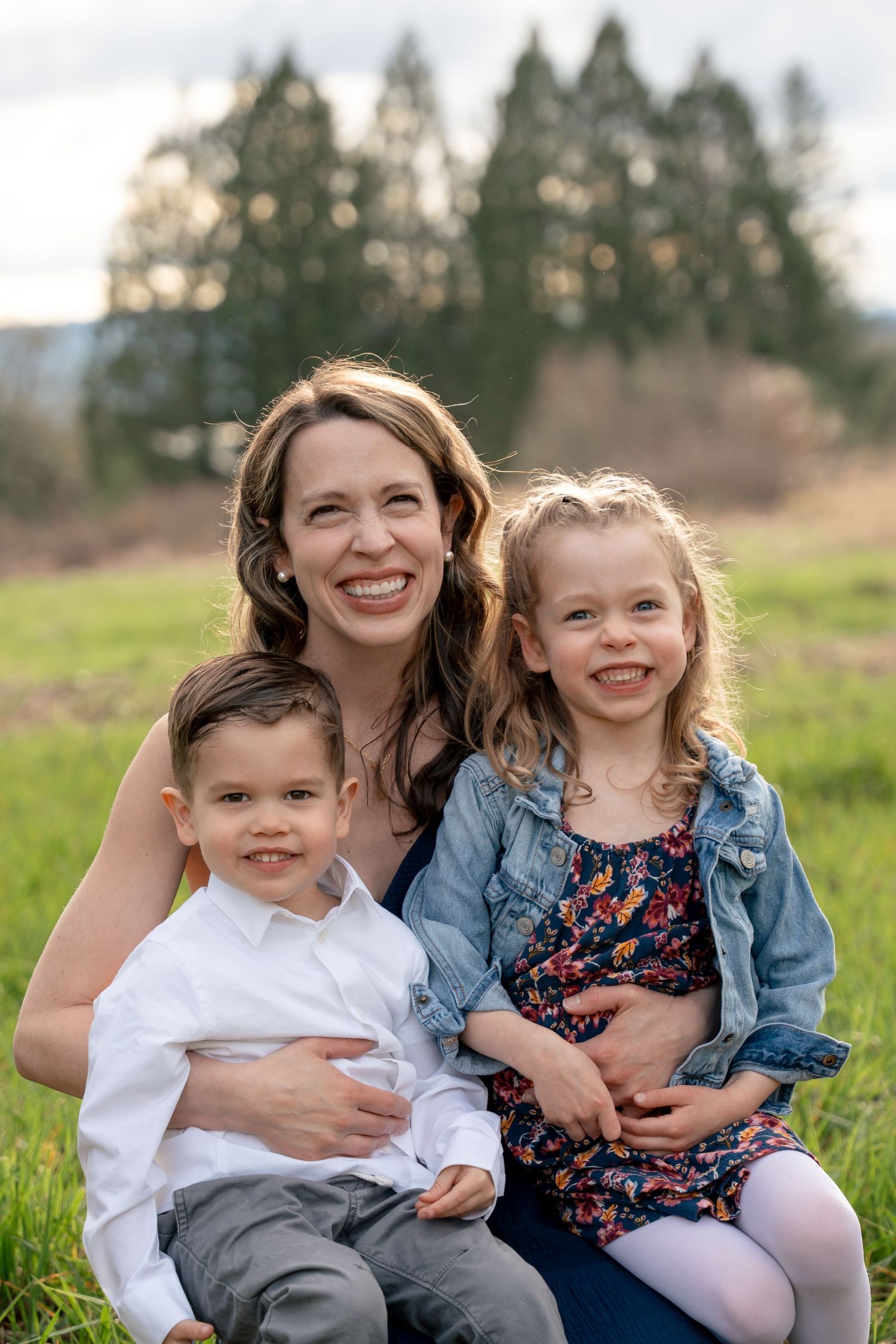 Smiling mother sits outdoors on green grass with her young son and daughter.