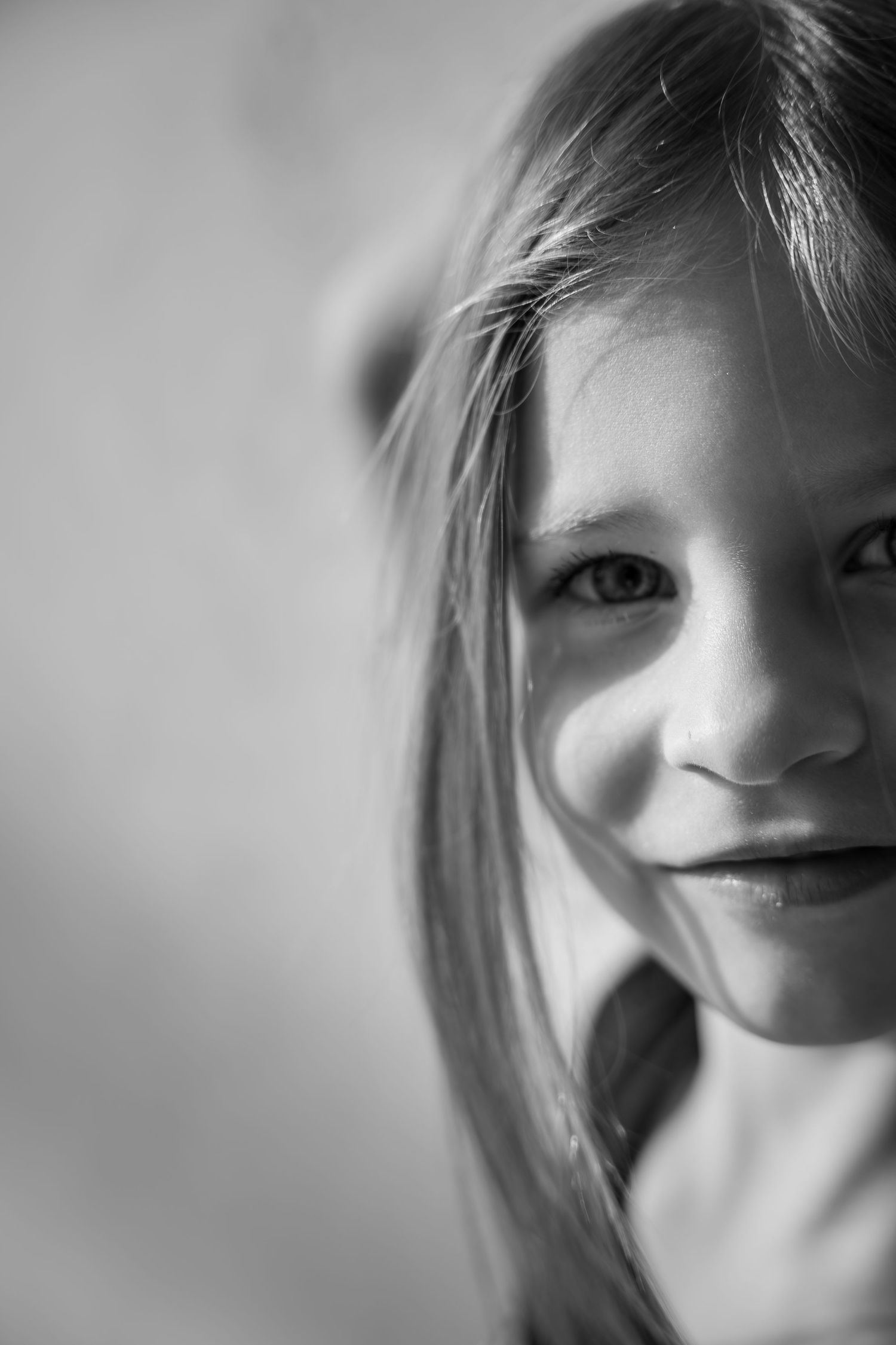 Black and white portrait of a smiling young girl with long hair, half-face close-up shot.