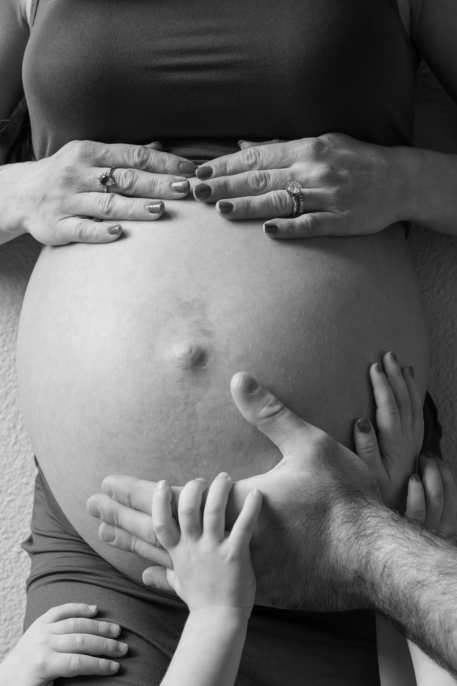 Black and white close-up of family hands lovingly cradling pregnant belly together.