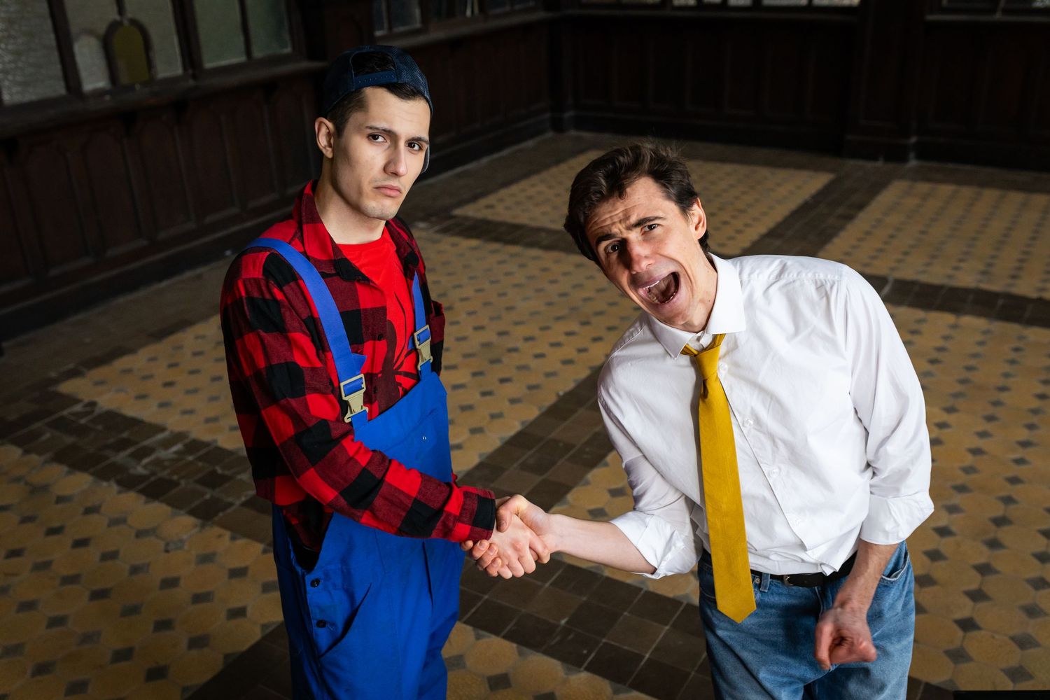 Two men shaking hands, one in blue overalls and red plaid shirt, other in white shirt and yellow tie.