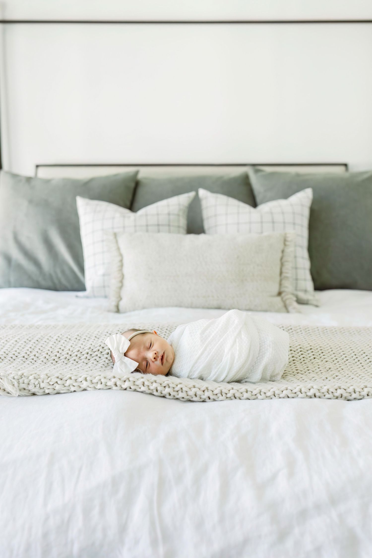 Peaceful newborn baby swaddled in white blanket sleeping on gray and white bedding.