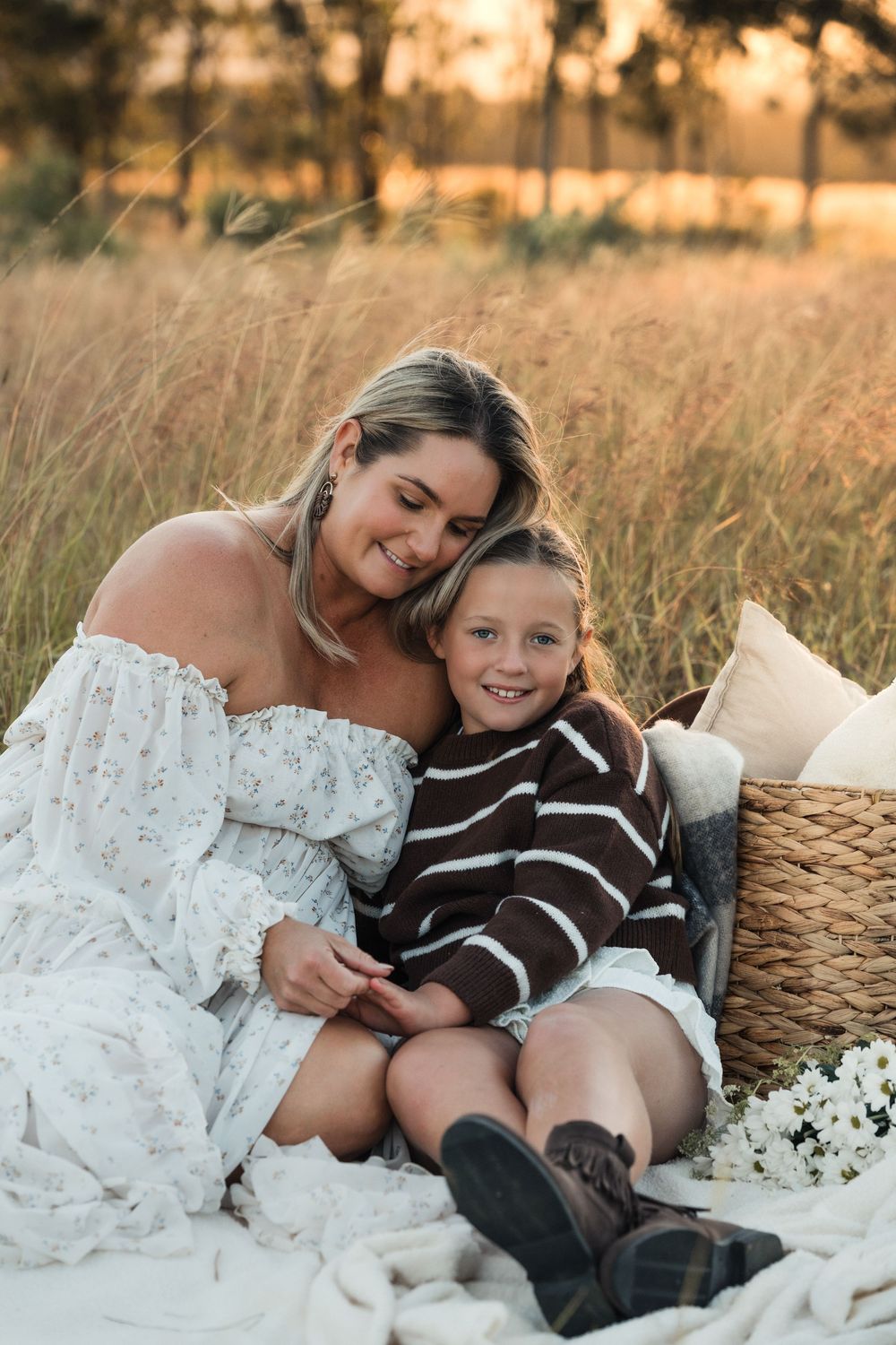 Mother and young son sitting together on a blanket in a golden field.