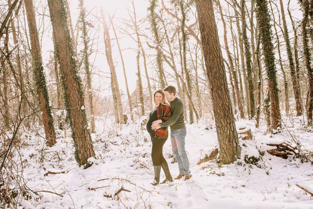 Winter engagement photoshoot in a snowy forest with soft natural lighting.