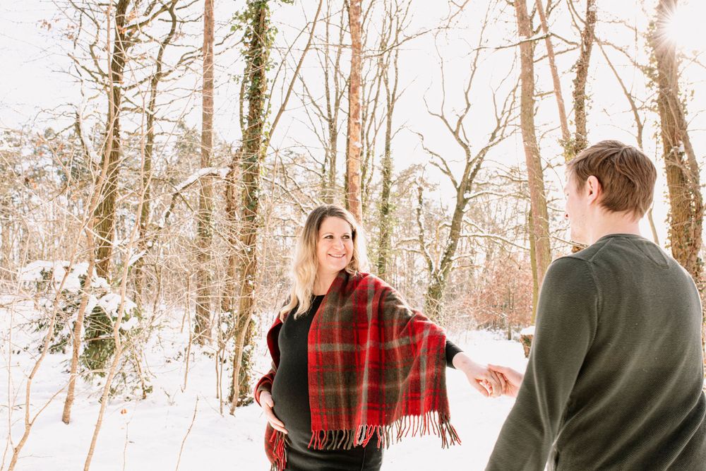 Couple walking through snowy woods wearing red plaid scarves and winter coats.