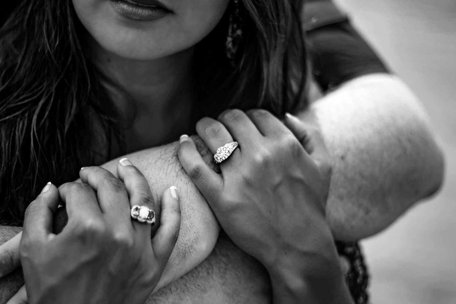 Close-up black and white photo of couple's hands intertwined, showcasing elegant engagement and wedding rings.