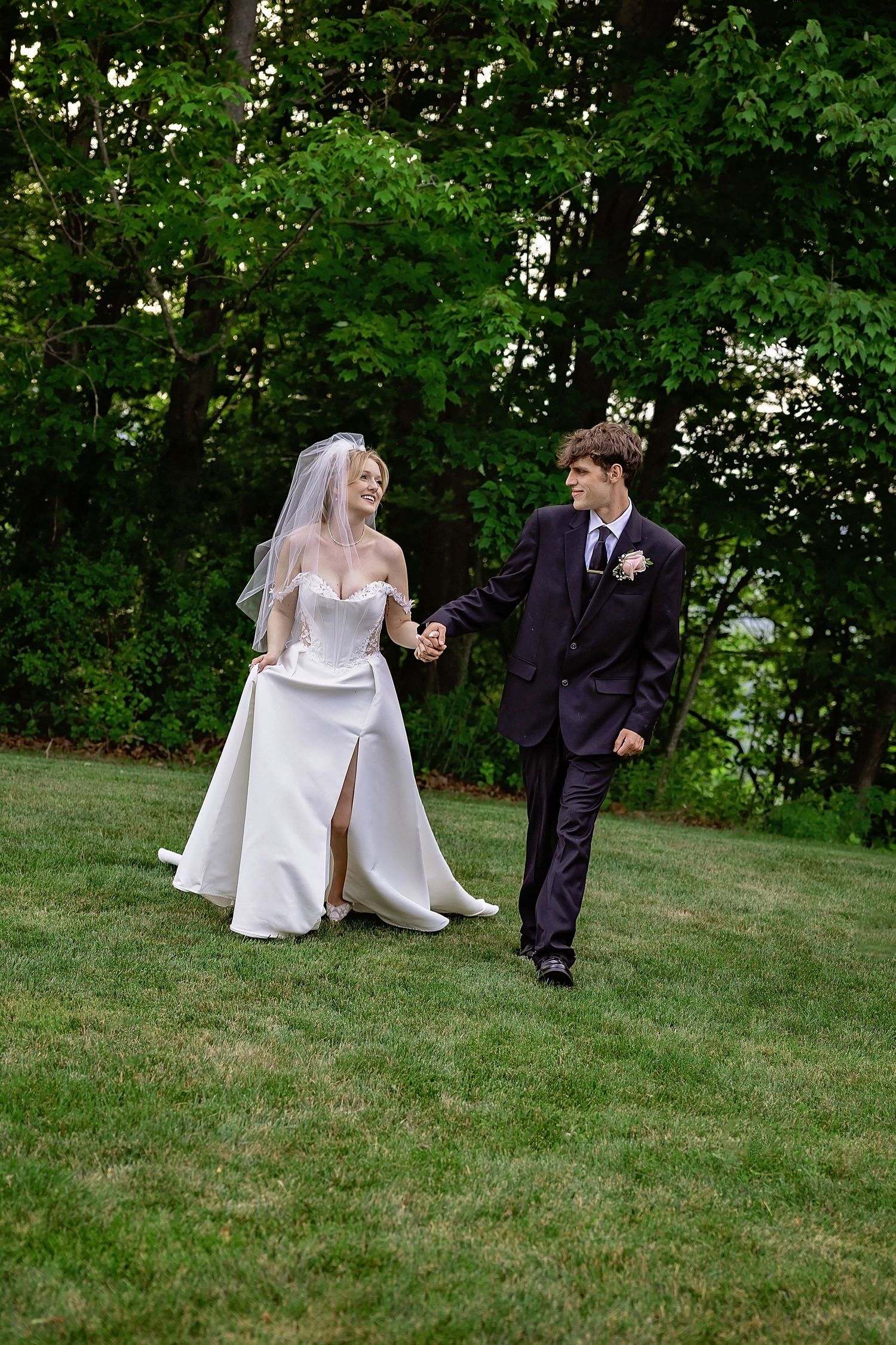 Bride and groom walking hand in hand across green lawn during outdoor summer wedding photography.
