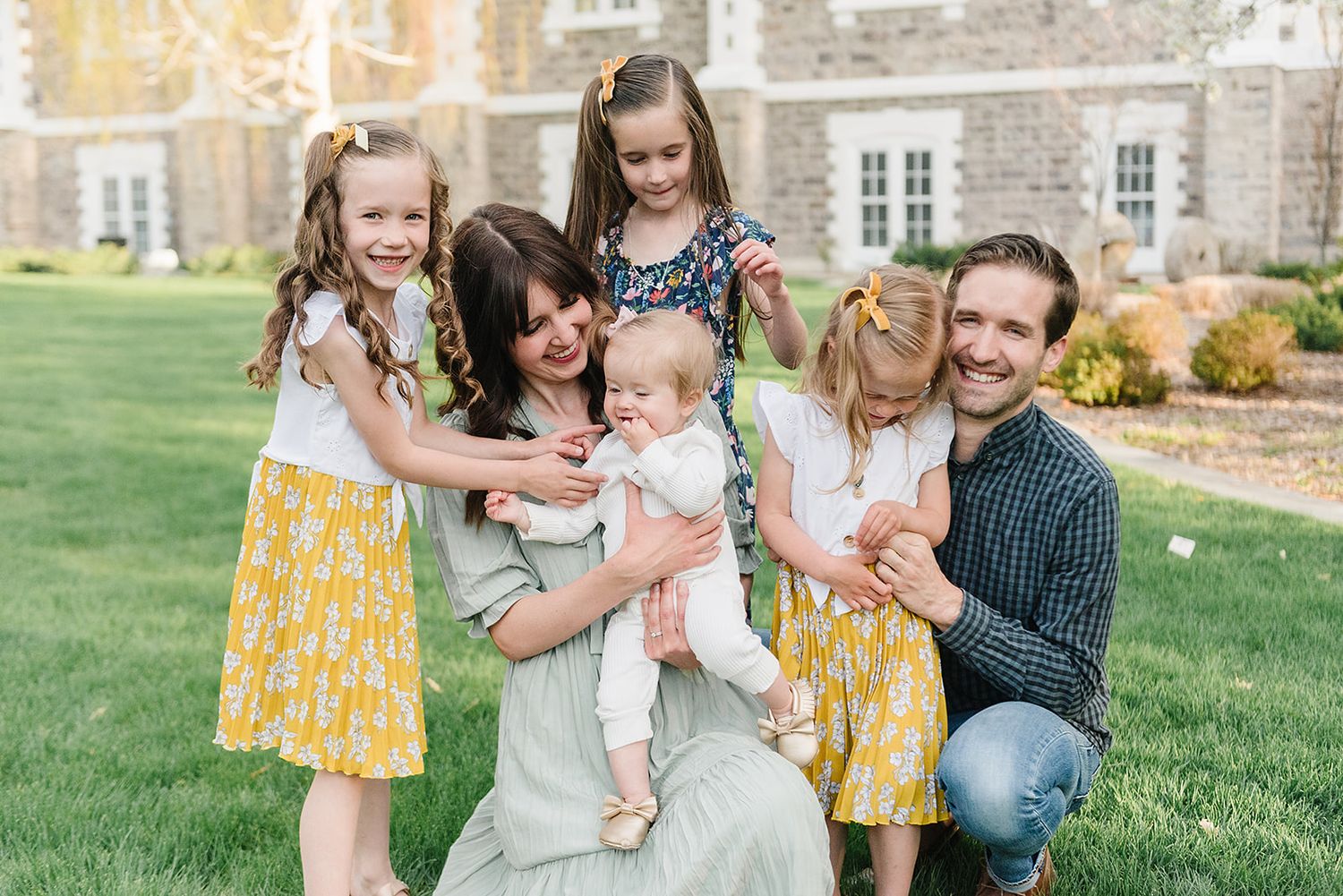 Candid outdoor family photo on grass with historic building in background.