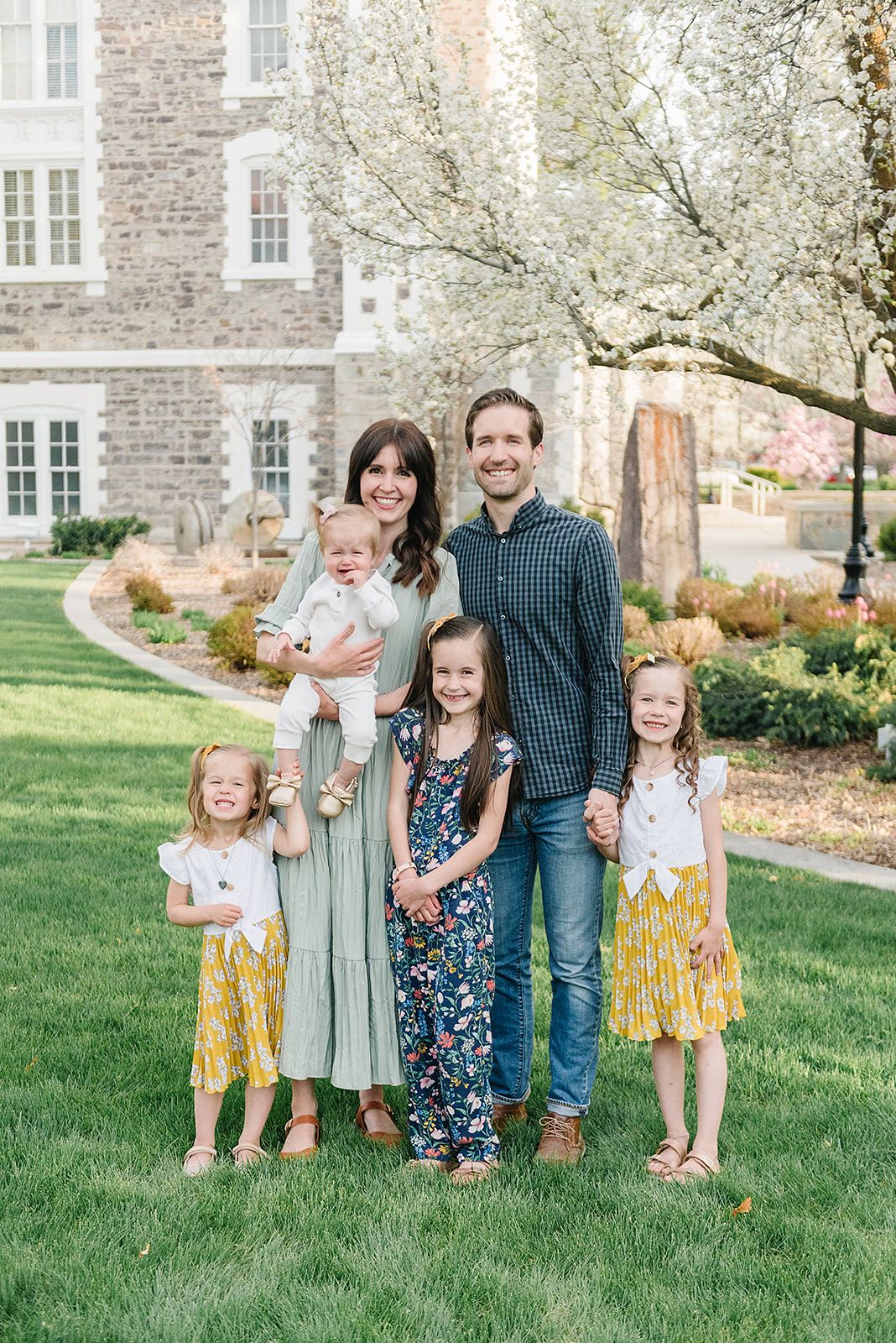 Spring family portrait with blooming white cherry trees and stone building backdrop.