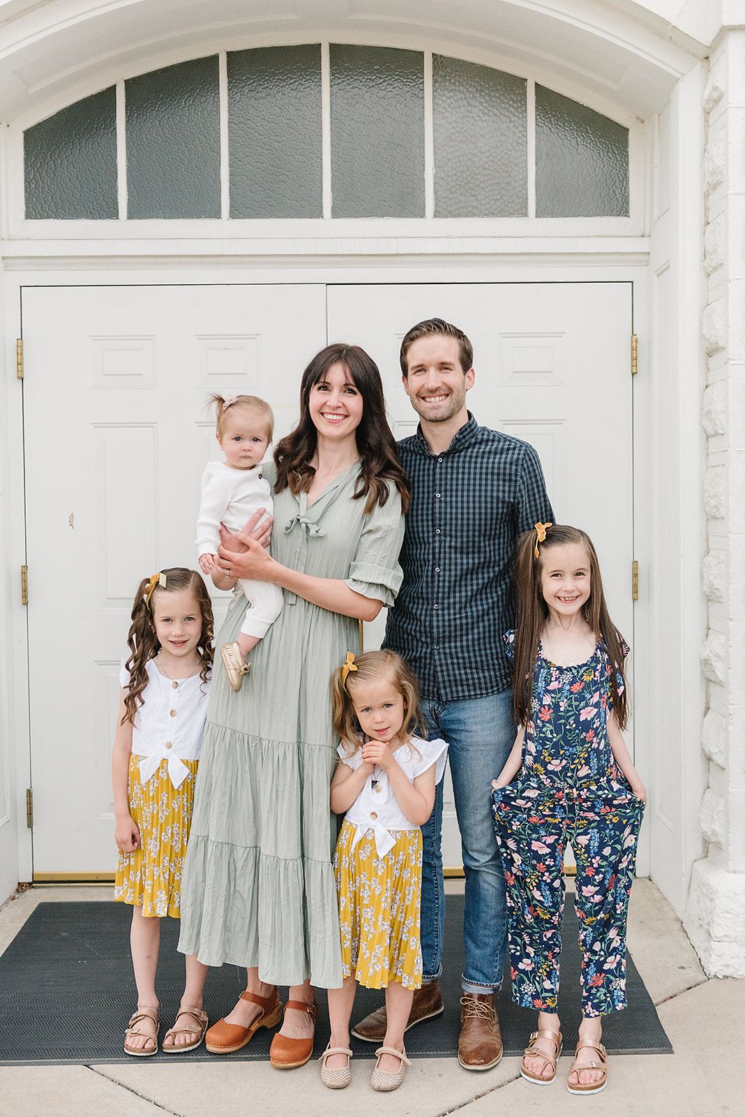 Family portrait in front of white doorway with young children in coordinated spring outfits.