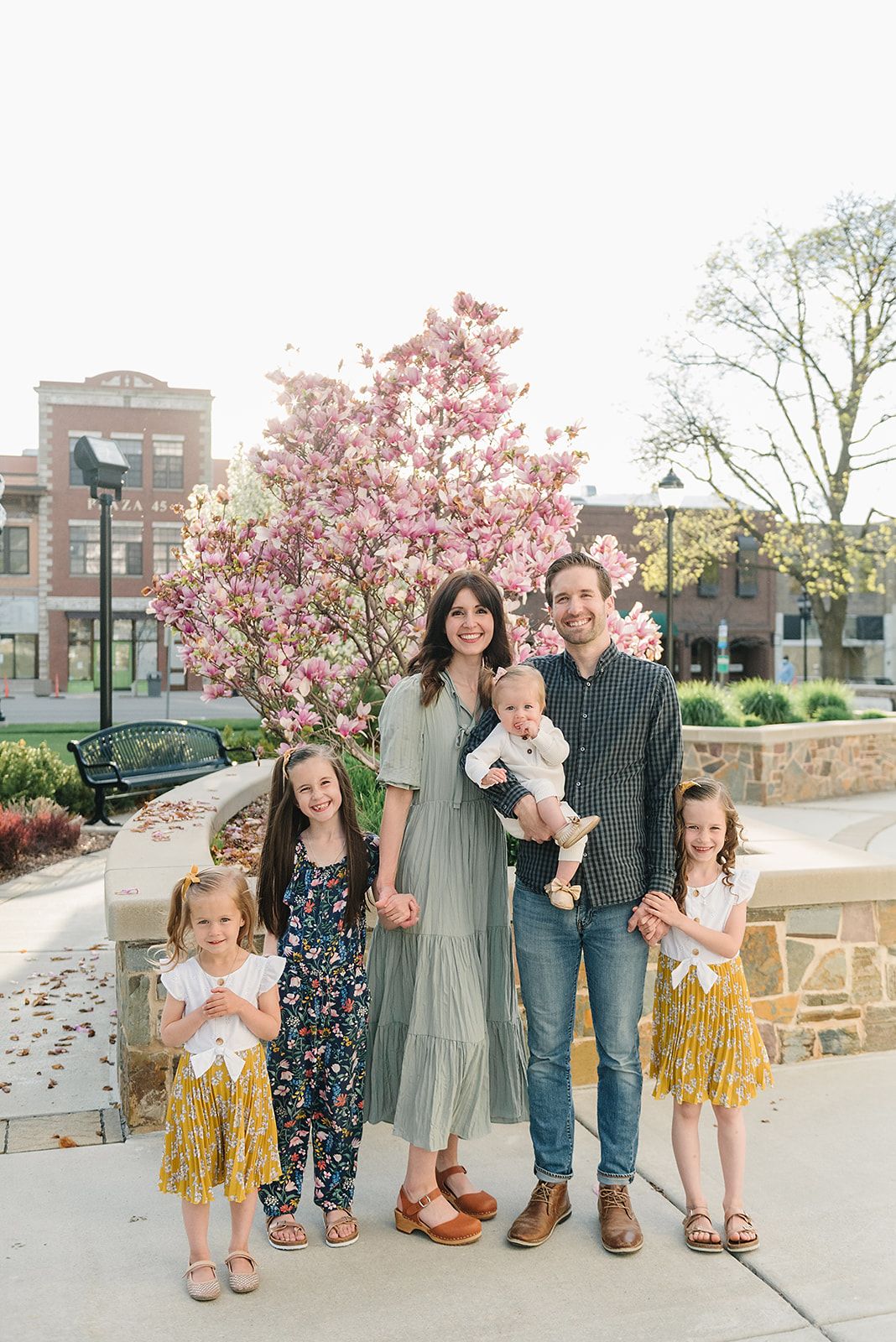 Family standing together under blooming pink magnolia tree in an urban setting.