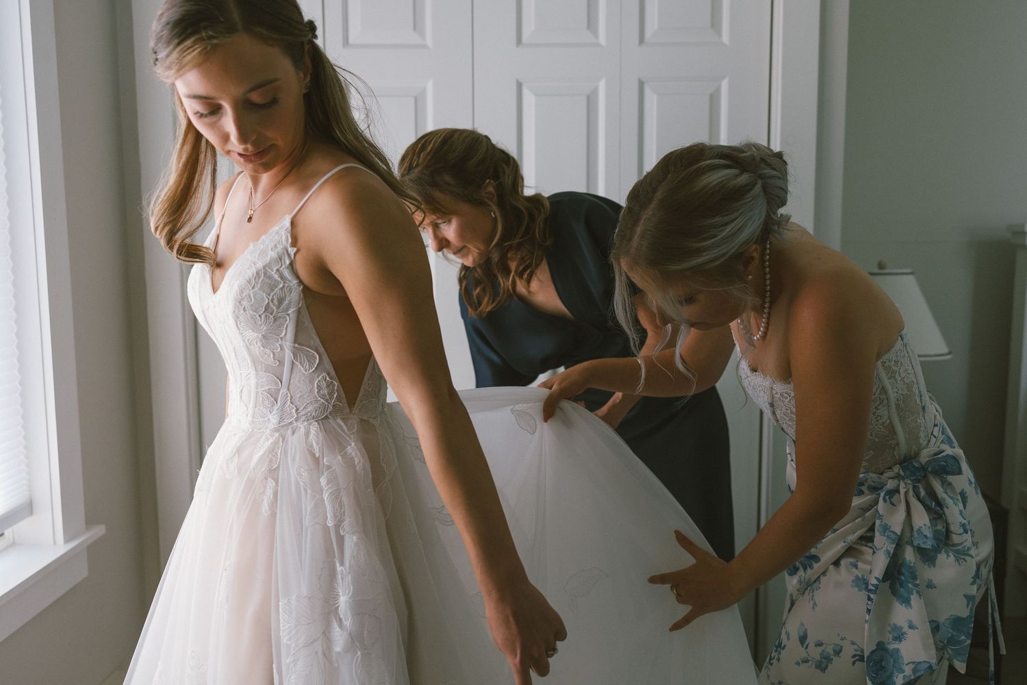 Getting ready scene with wedding dress preparations in a sunlit room.