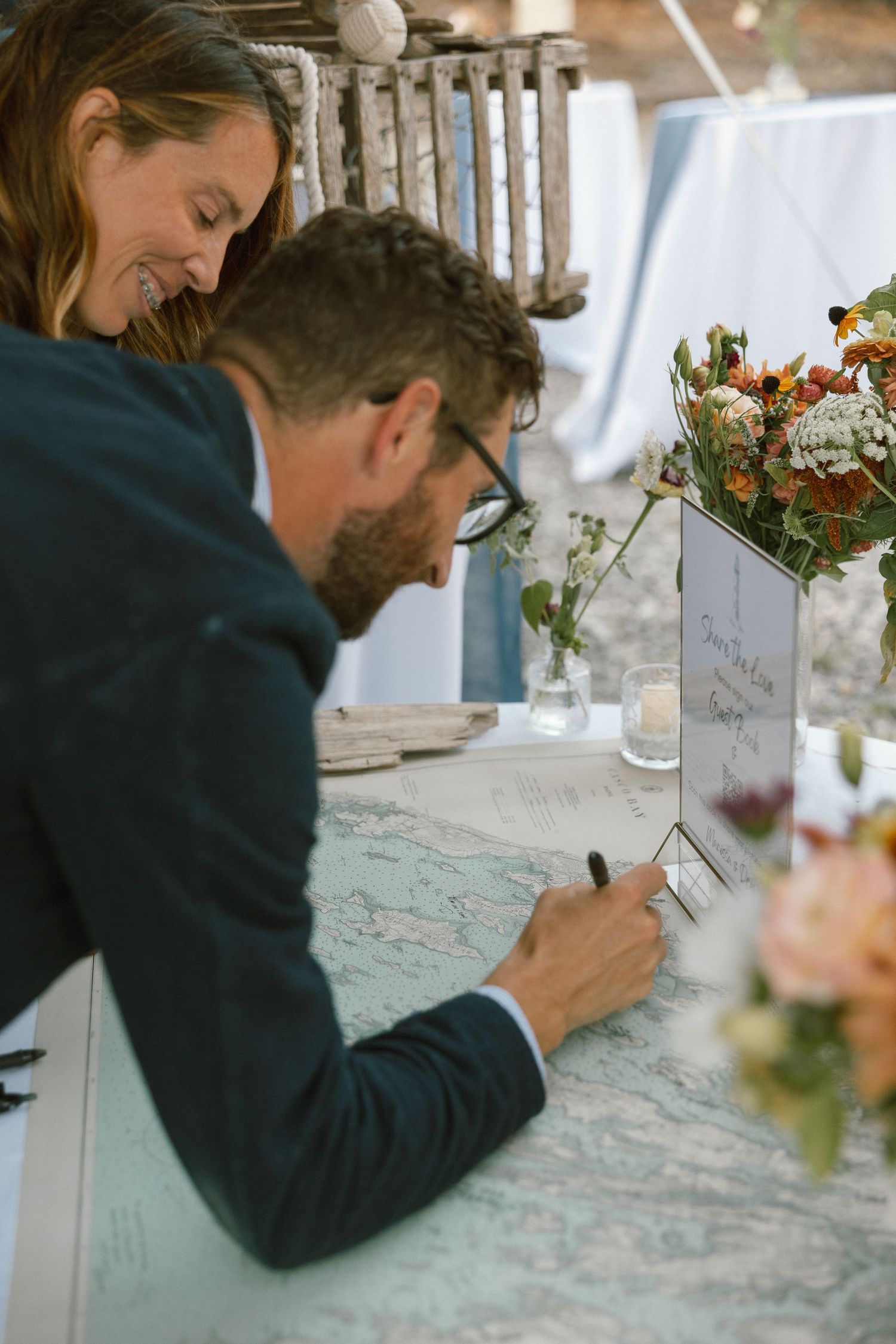 Guest signing book at wedding reception with floral centerpieces on table.