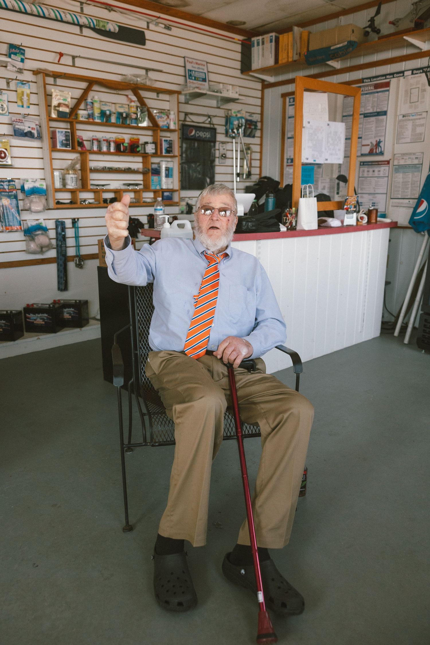 Elderly person sitting in a chair with a cane in an office setting with wooden paneled walls.