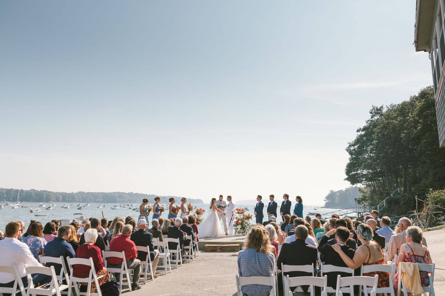 Wedding guests seated in white chairs overlooking a scenic waterfront.
