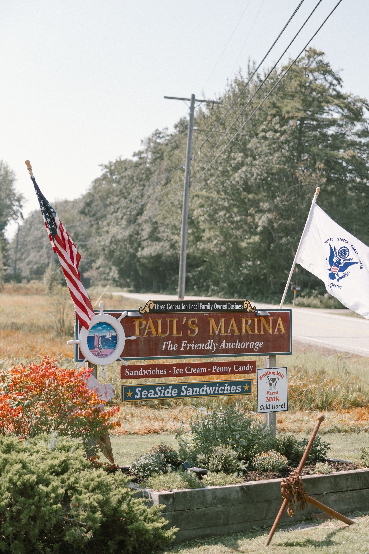 Paul's Marina entrance sign with American flags and orange flowers.