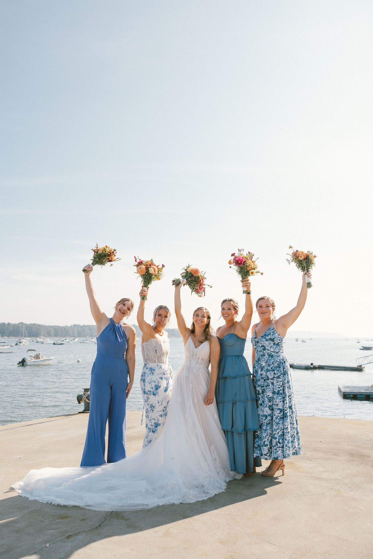 Wedding party in blue and white dresses posing on a seaside dock.