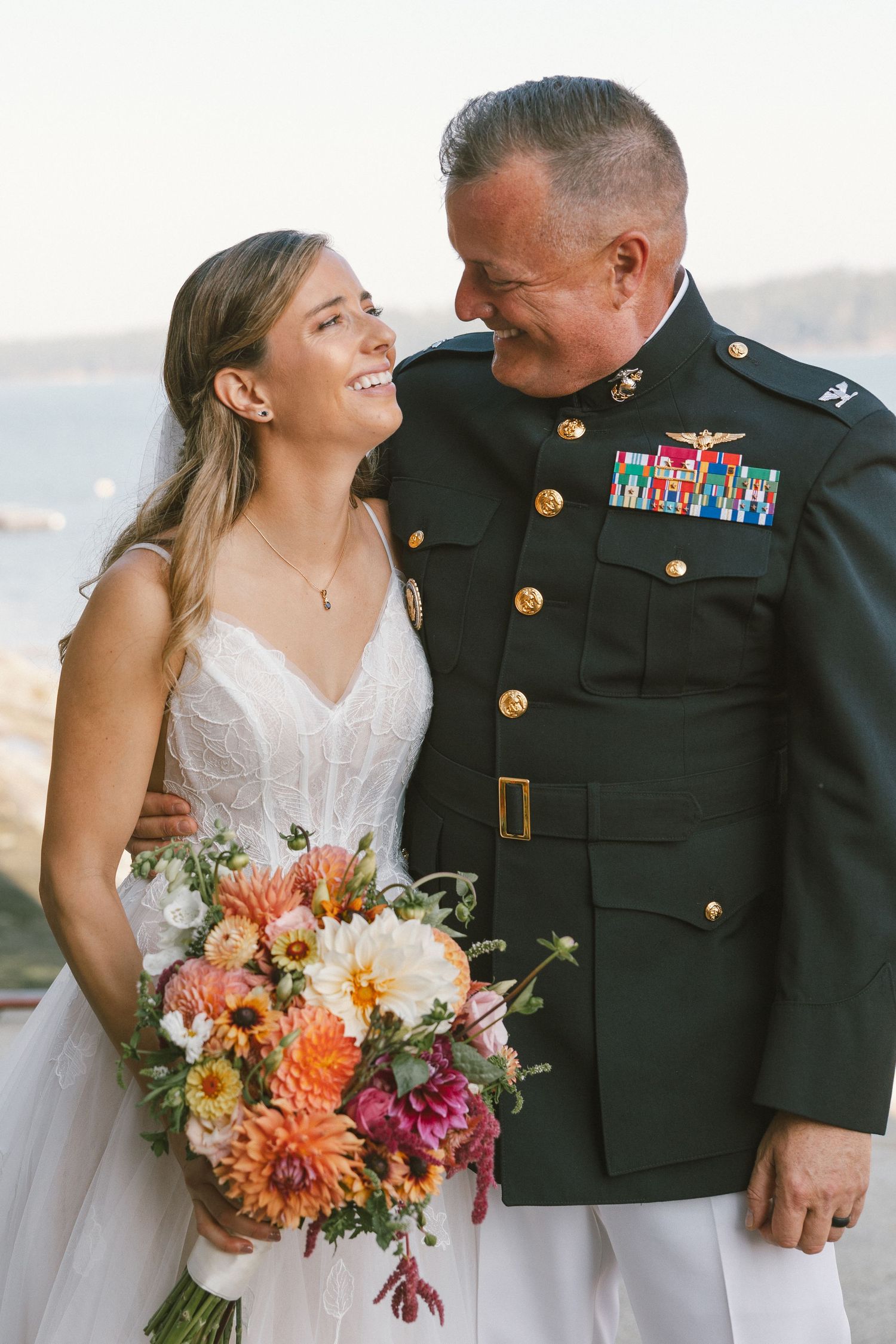 Military wedding couple with vibrant autumn bouquet by the water.