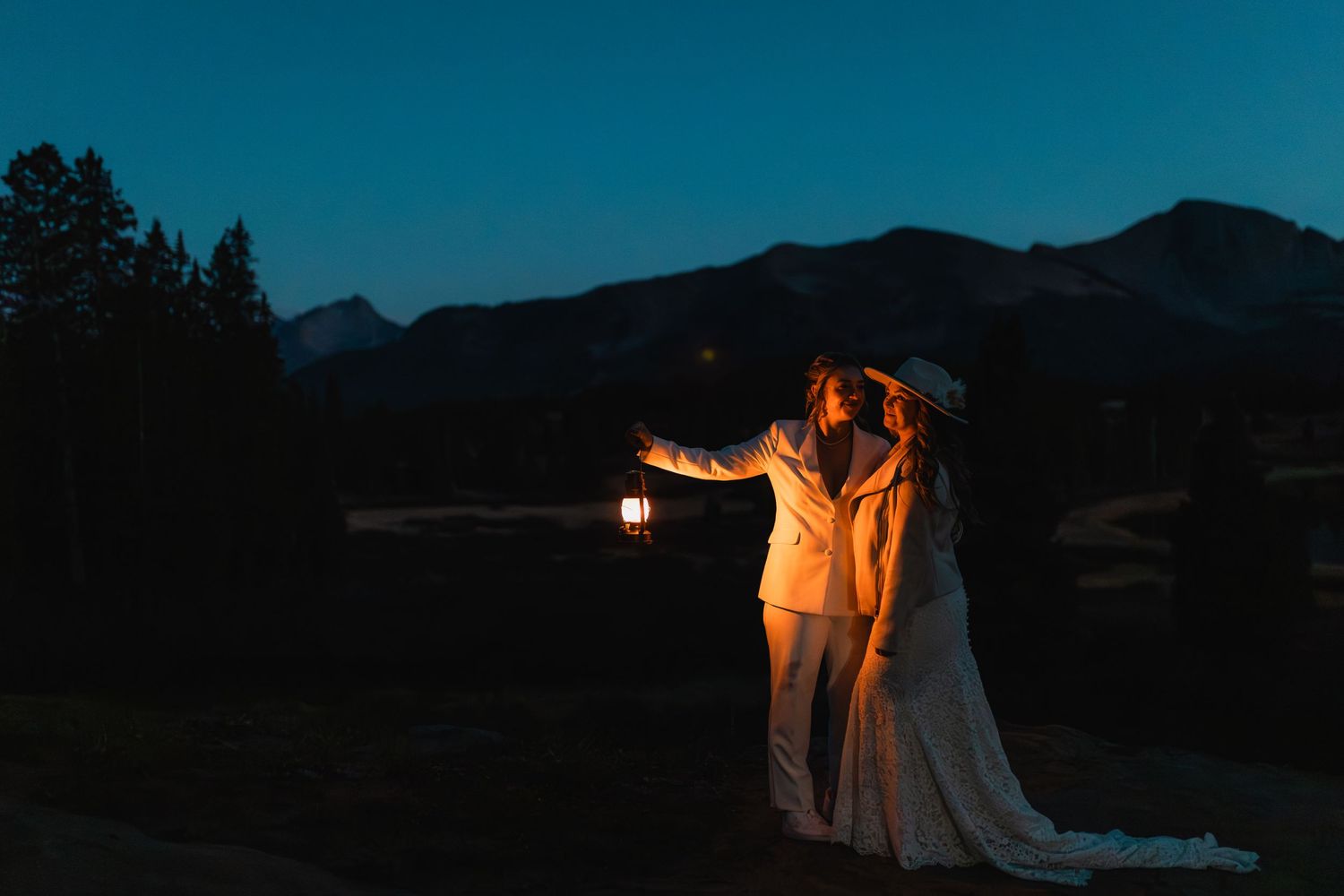 Two silhouettes holding a lantern stand against a mountain backdrop at dusk with a dramatic glowing light effect.