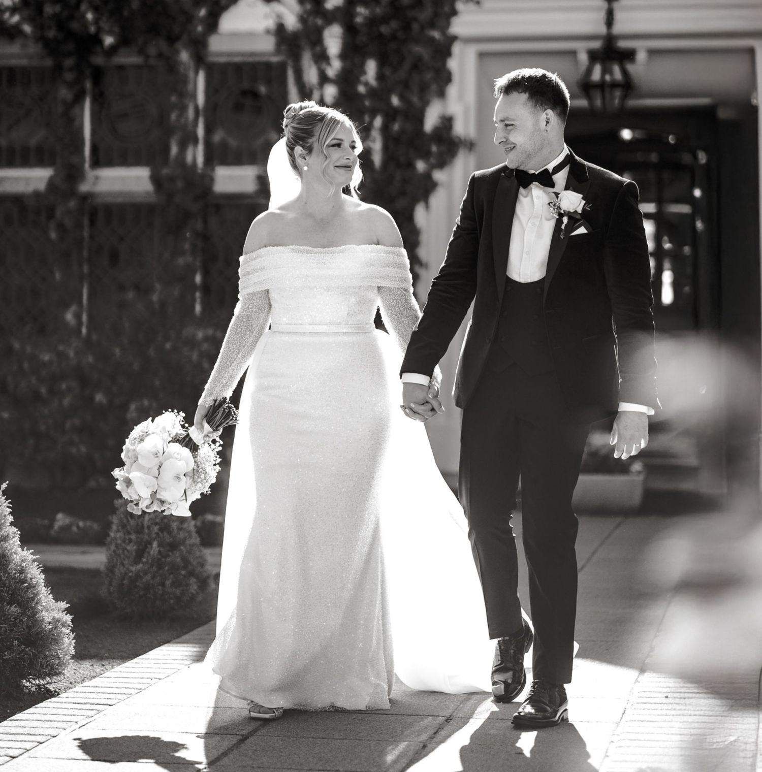 A newlywed couple walks down stone church steps together holding hands, with the bride in white and groom in classic tuxedo.