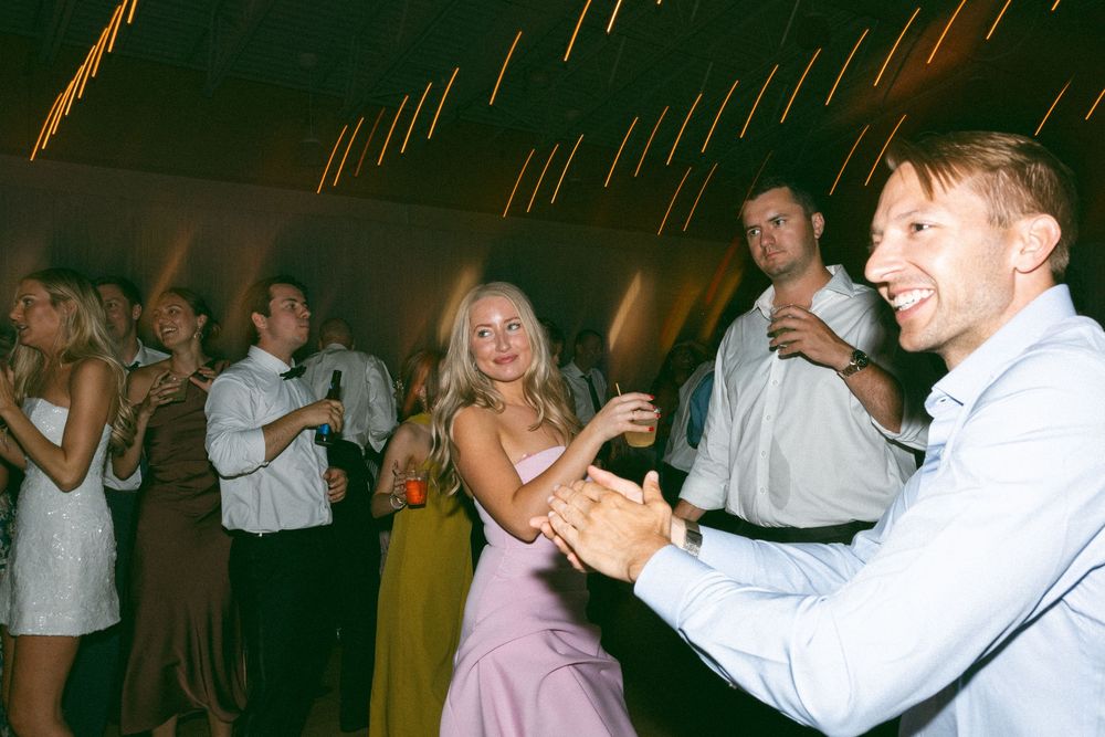 Guests dancing and laughing at a wedding reception inside a warmly lit venue.