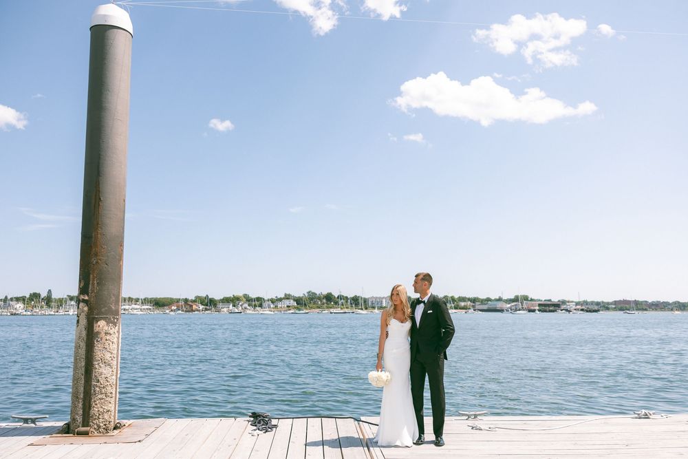 Bride and groom share a romantic kiss on a wooden dock by the water on their sunny wedding day.