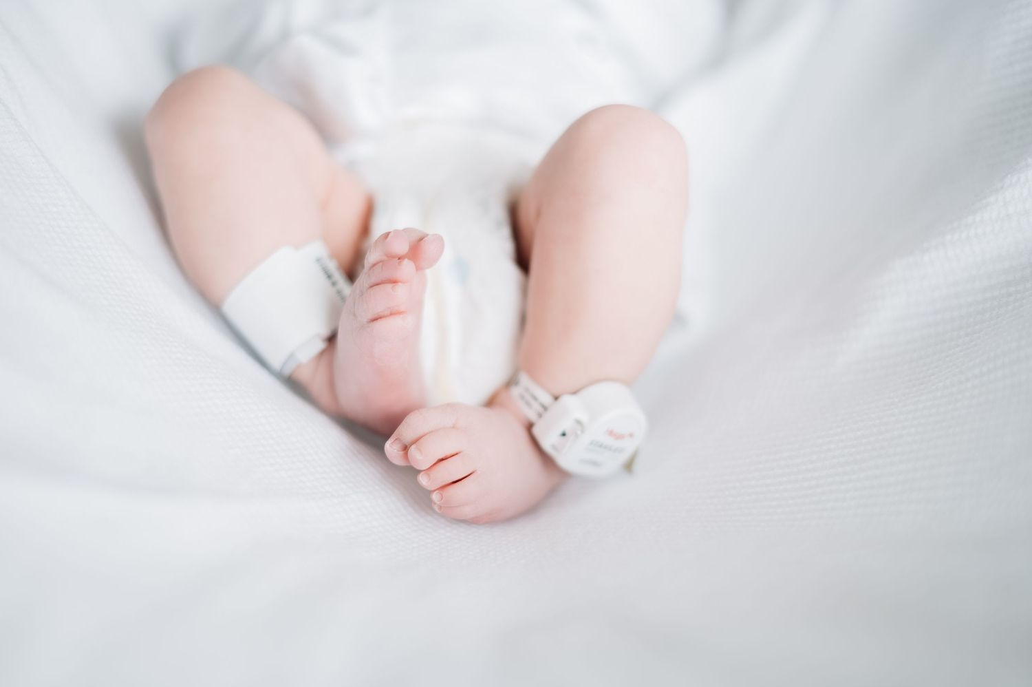 Baby's tiny feet wrapped in white fabric against light background.