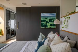 A modern bedroom interior with white bedding, dark accent walls, and large windows overlooking a scenic landscape.
