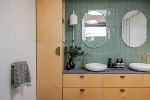A modern bathroom interior features light wood walls, green tile accents, and circular mirrors above a floating vanity.