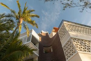 Modern architectural detail with geometric patterns and palm tree against blue sky in warm sunlight.