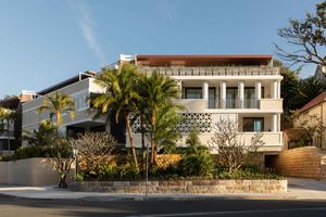 Modern white two-story house with palm trees and stone retaining wall along a coastal street.